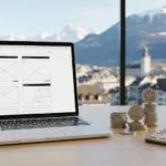 A laptop showing a website wireframe on a desk with Swiss franc coins, illustrating the planning and cost of website development in Switzerland for 2025.